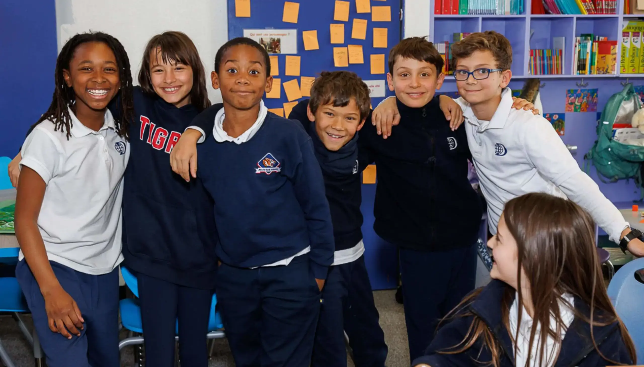 Group of DIS students smiling arm in arm with friends in a classroom.