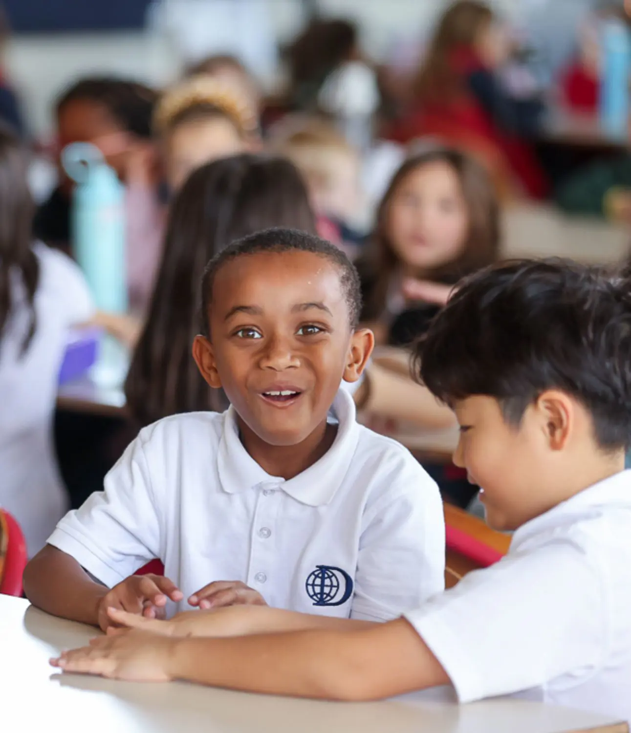 DIS Elementary school smiling with a friend while sitting at a table together.