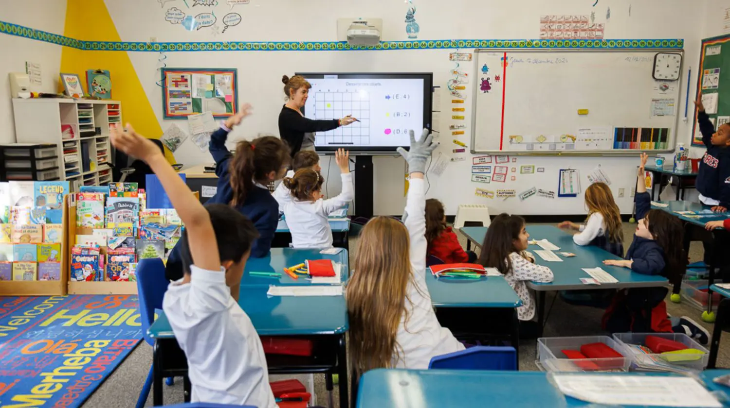 Elementary School students putting their hands up to answer a question in class.