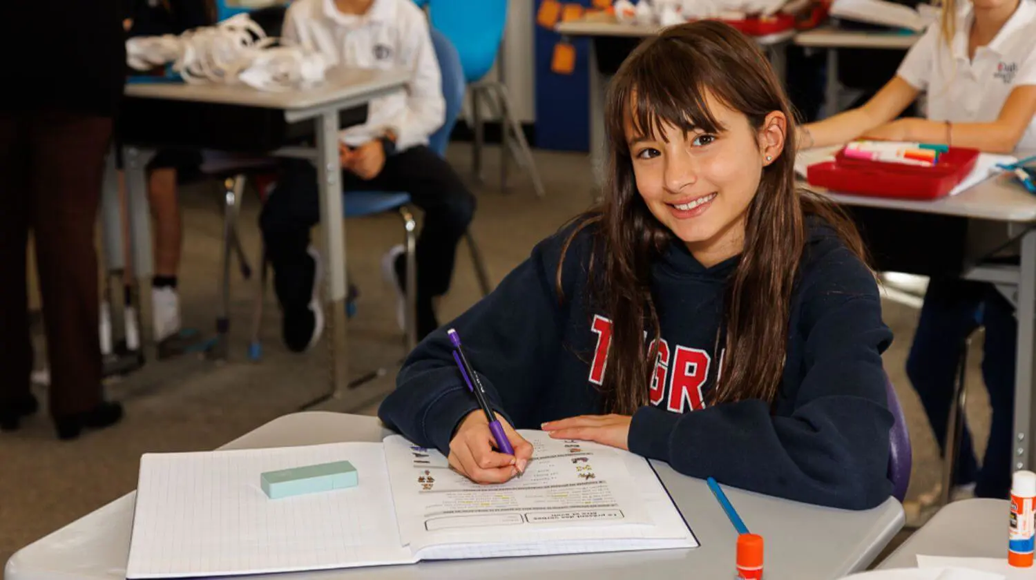 DIS Elementary School student smiling while completing a worksheet in a class.