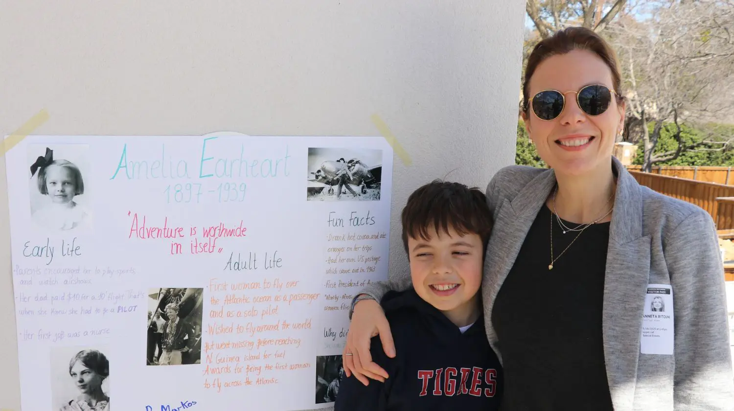 Parent and child smiling for a photo with a hand-made poster about Amelia Earheart.