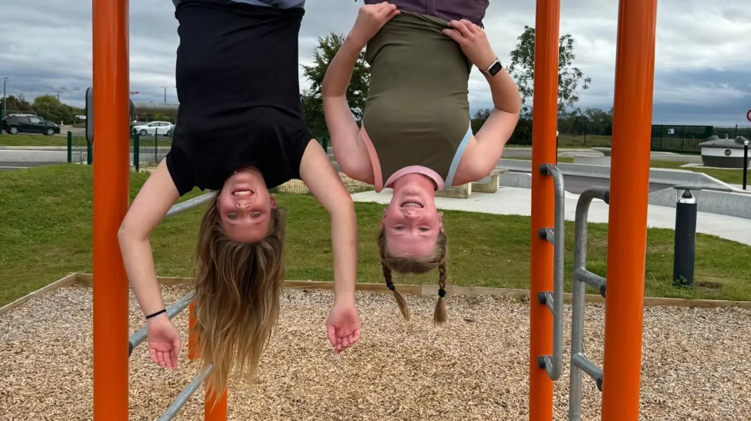 DIS students hanging upside down from a climbing frame and grinning.