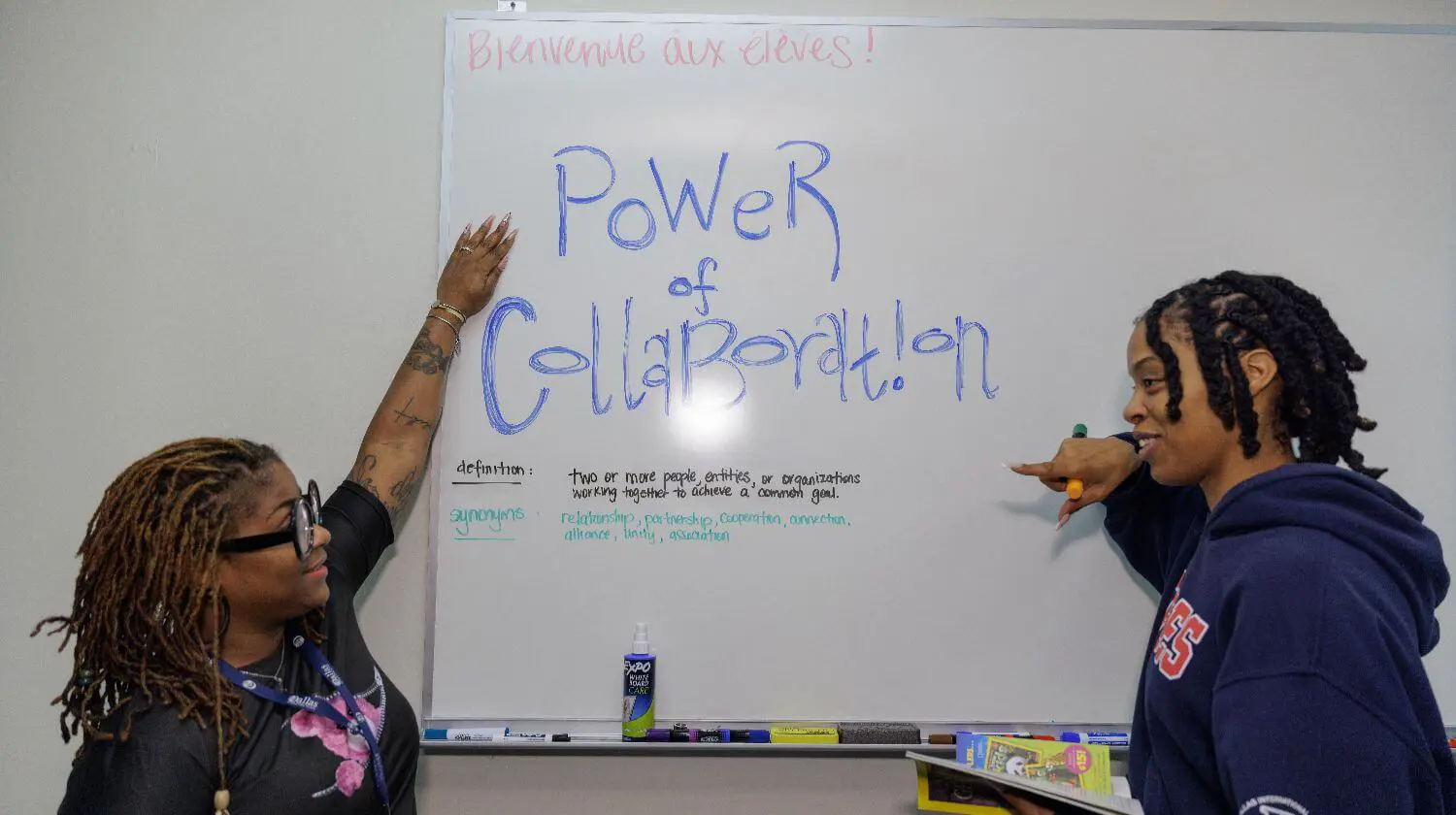 Teacher and student point at whiteboard which reads 'Power of Collaboration'.